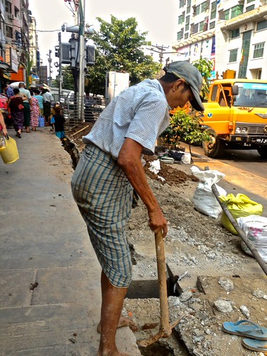 Workers digging what may be a hole for a pipe, barefoot. Kids included (see the upper ditch)