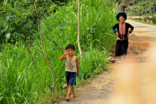 a young boy waves as we pass him and his grandmother in Black Hmong traditional dress